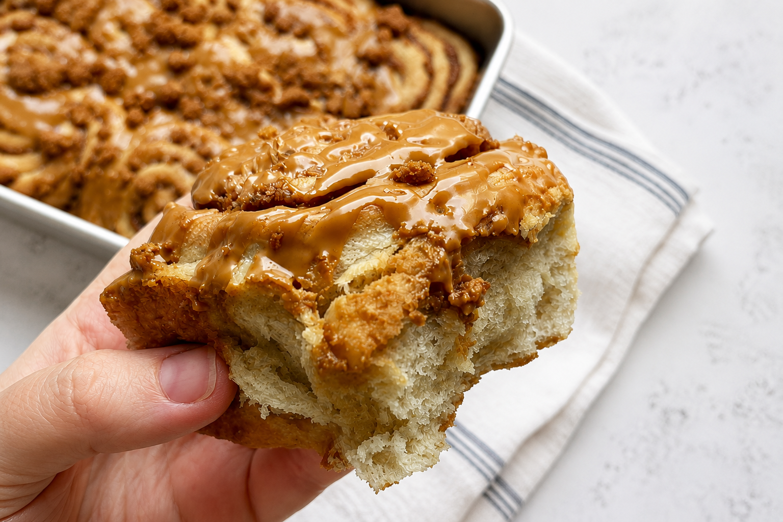 A freshly baked vegan cinnamon roll held above a tray