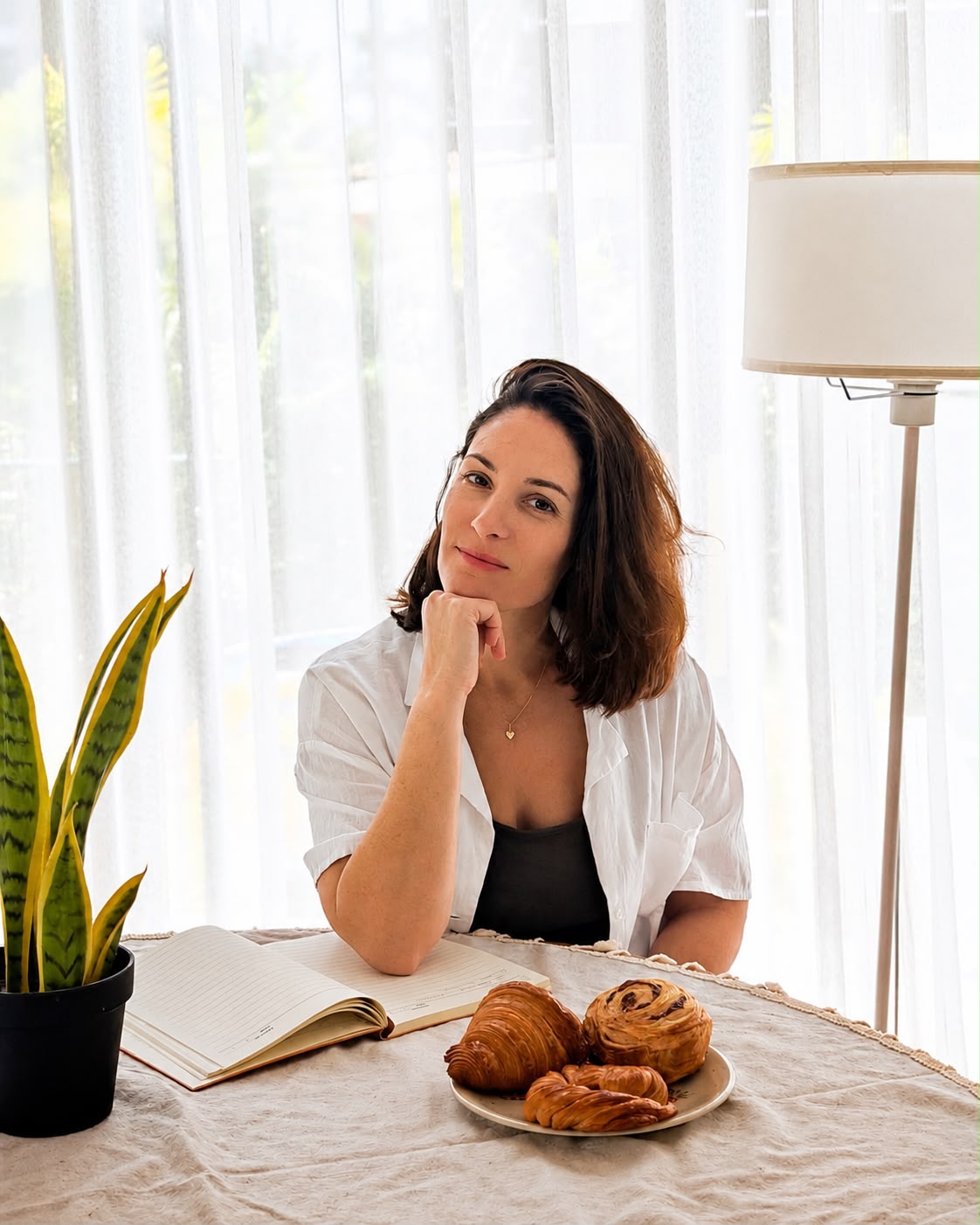 Danielle sitting at a table with a laptop, notebook, and a plate of croissants and cinnamon rolls